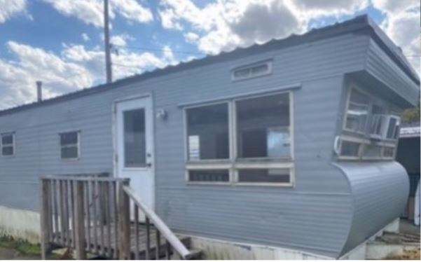 Vintage gray mobile home with window AC unit in as-is condition